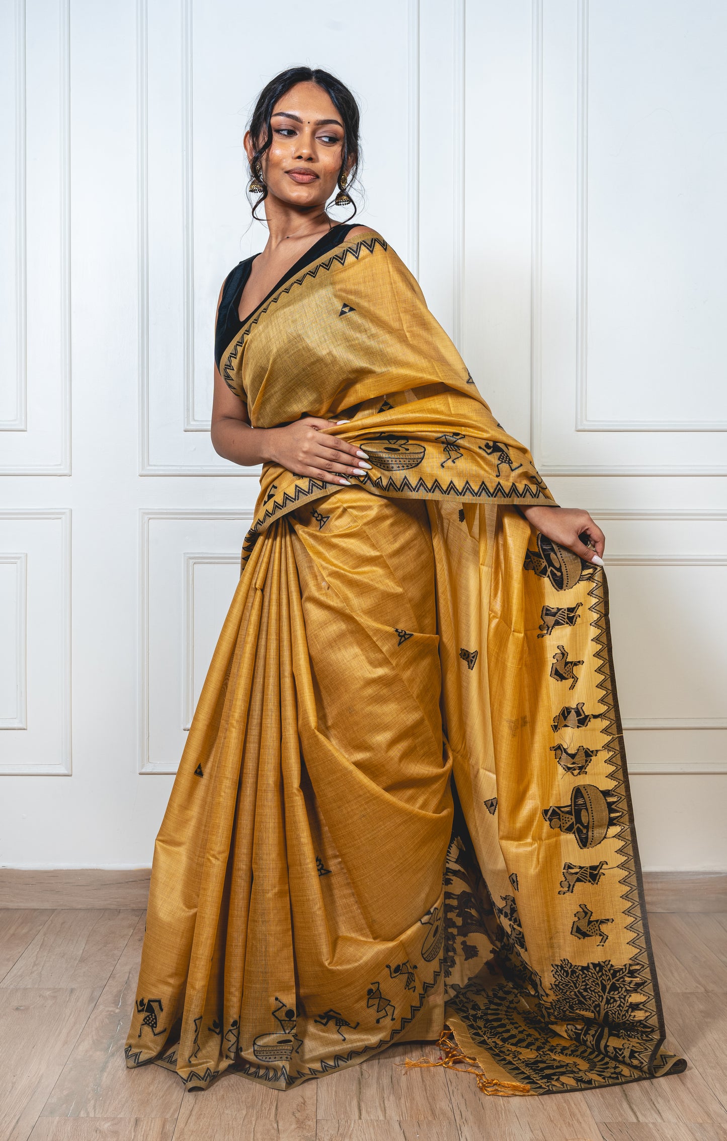 Sandalwood yellow cotton silk saree with black Warli-embroidered pallu and crisp pleats—capturing festive finesse and graceful drape