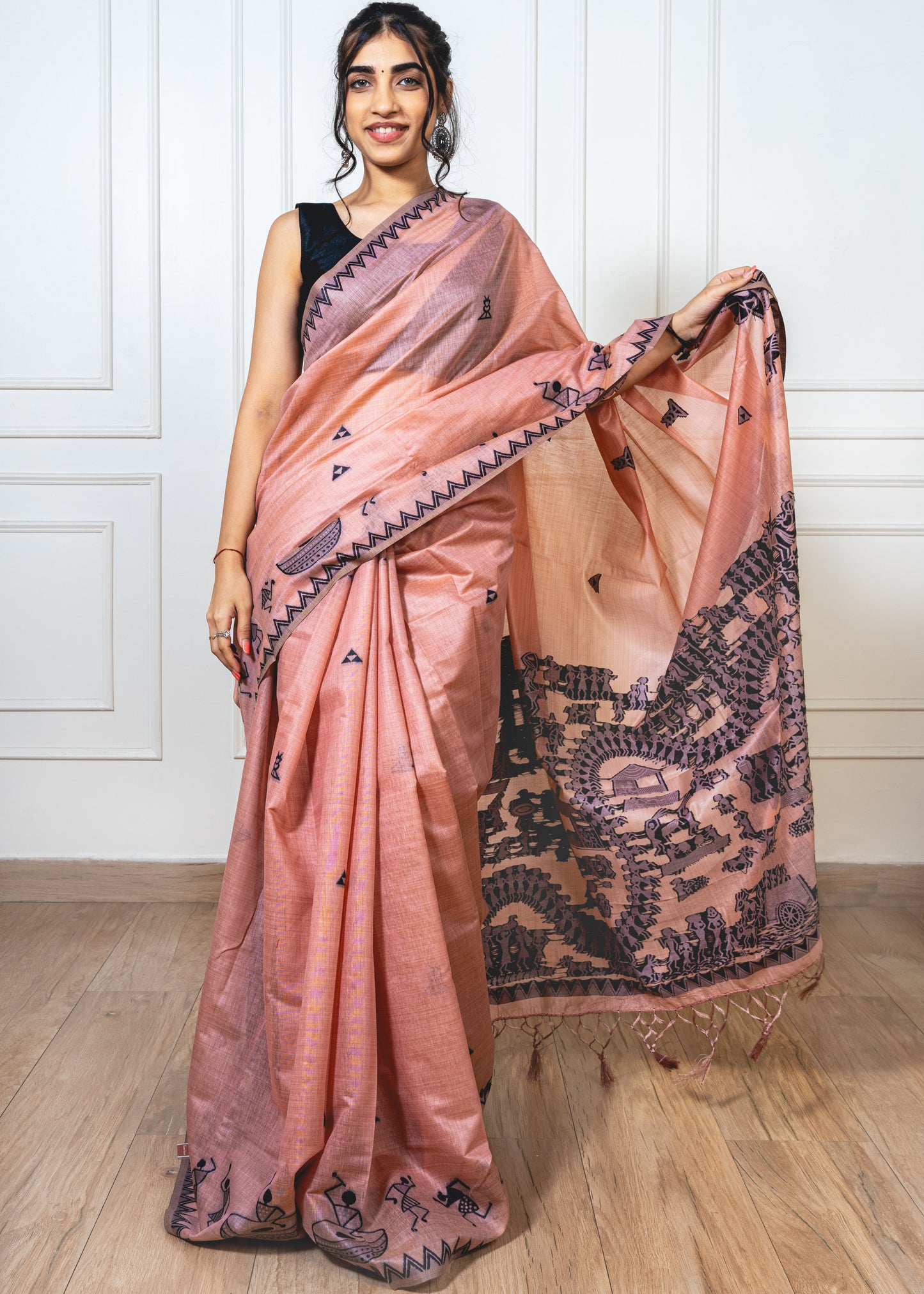 Woman wearing blush pink cotton silk saree with black Warli embroidery—styled for graceful movement and folk-inspired elegance.