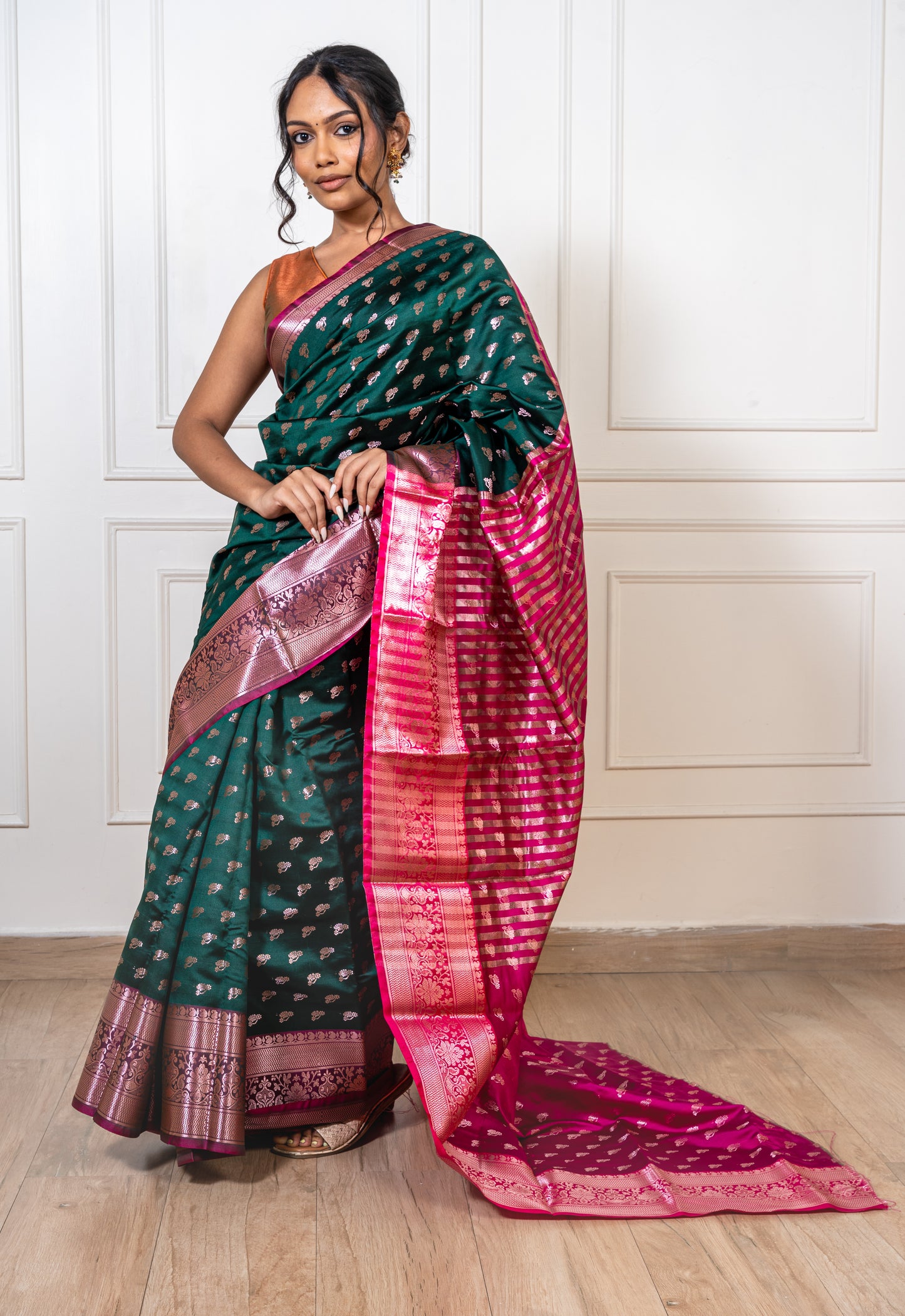 Peacock green saree laid flat—featuring golden zari motifs and contrast red border with rich, lustrous texture.