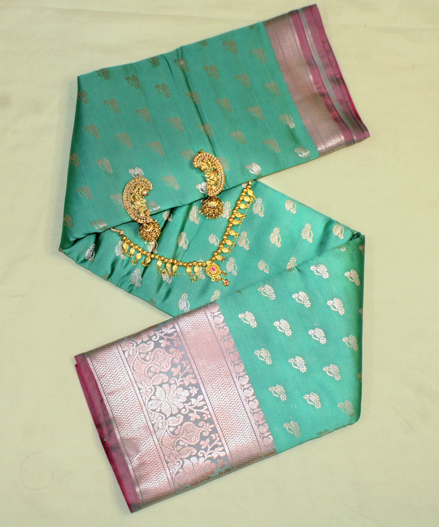 Close-up of golden zari on teal green semi silk saree—highlighting intricate craftsmanship and jewel-toned shimmer.