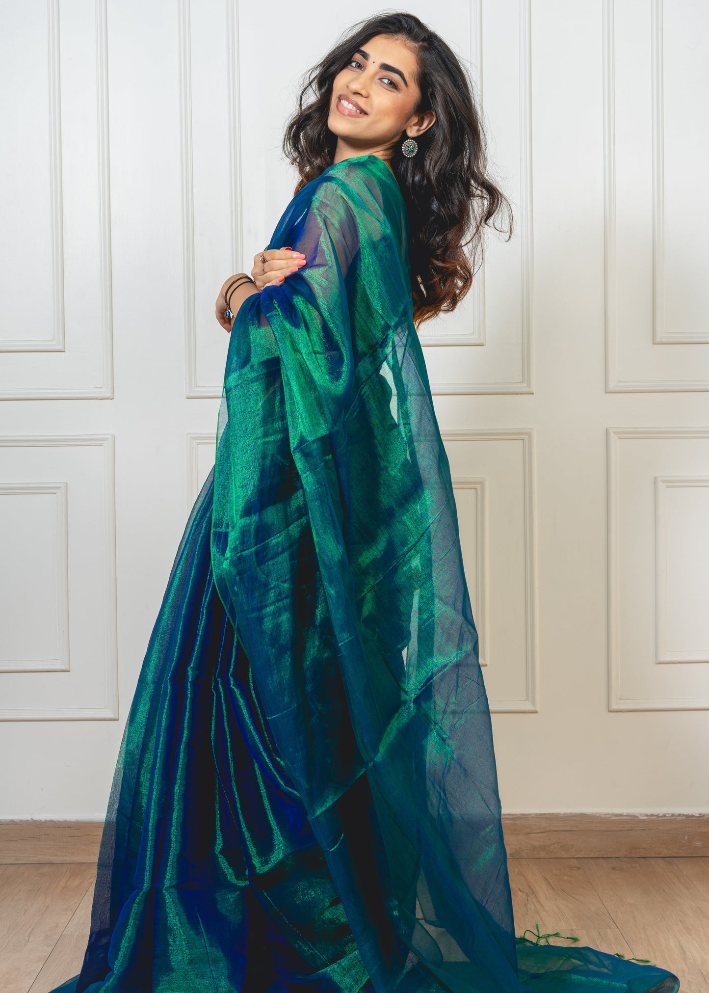 Woman wearing peacock green tissue silk saree without border—styled for festive evenings, graceful rituals, and timeless elegance.