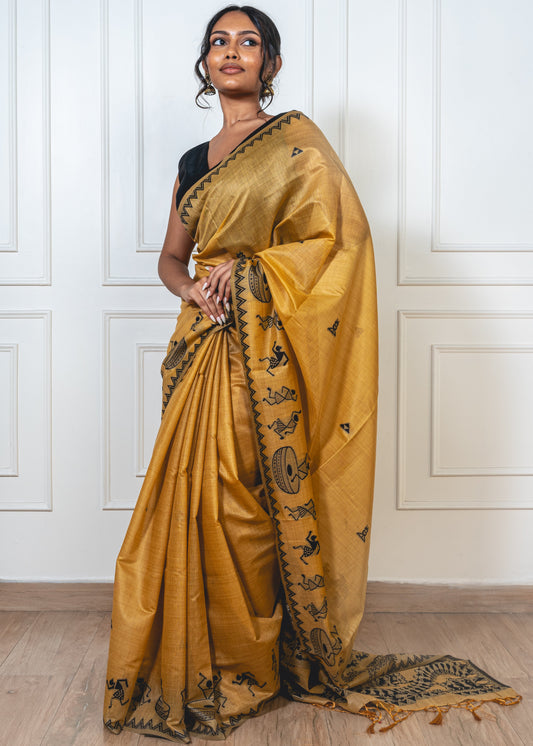 Woman wearing sandalwood yellow cotton silk saree with black Warli embroidery—styled for festive grace and folk-inspired elegance.