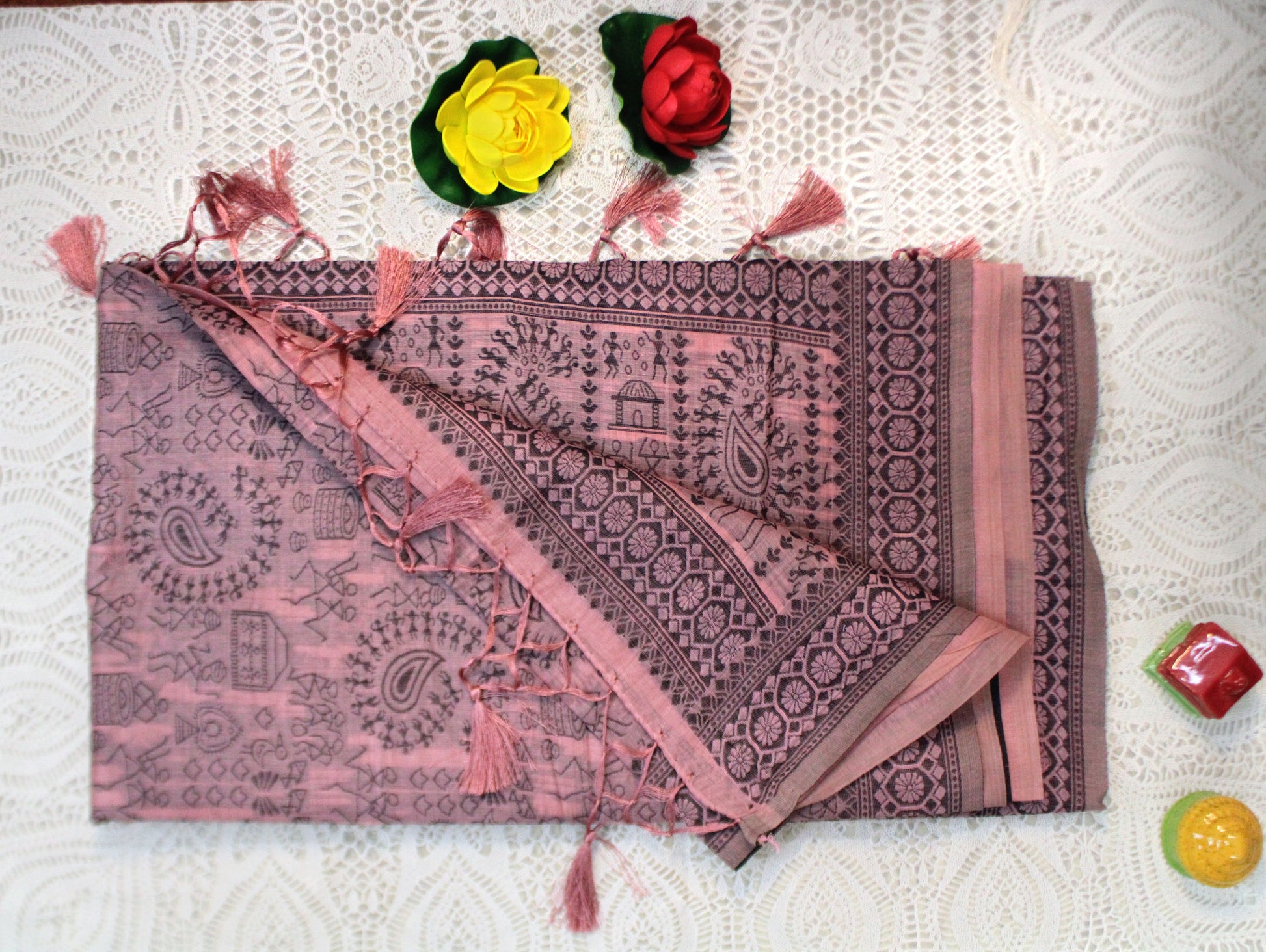 Soft pink cotton saree laid flat, showcasing Warli motifs and airy texture—crafted for subtle charm and cultural depth.